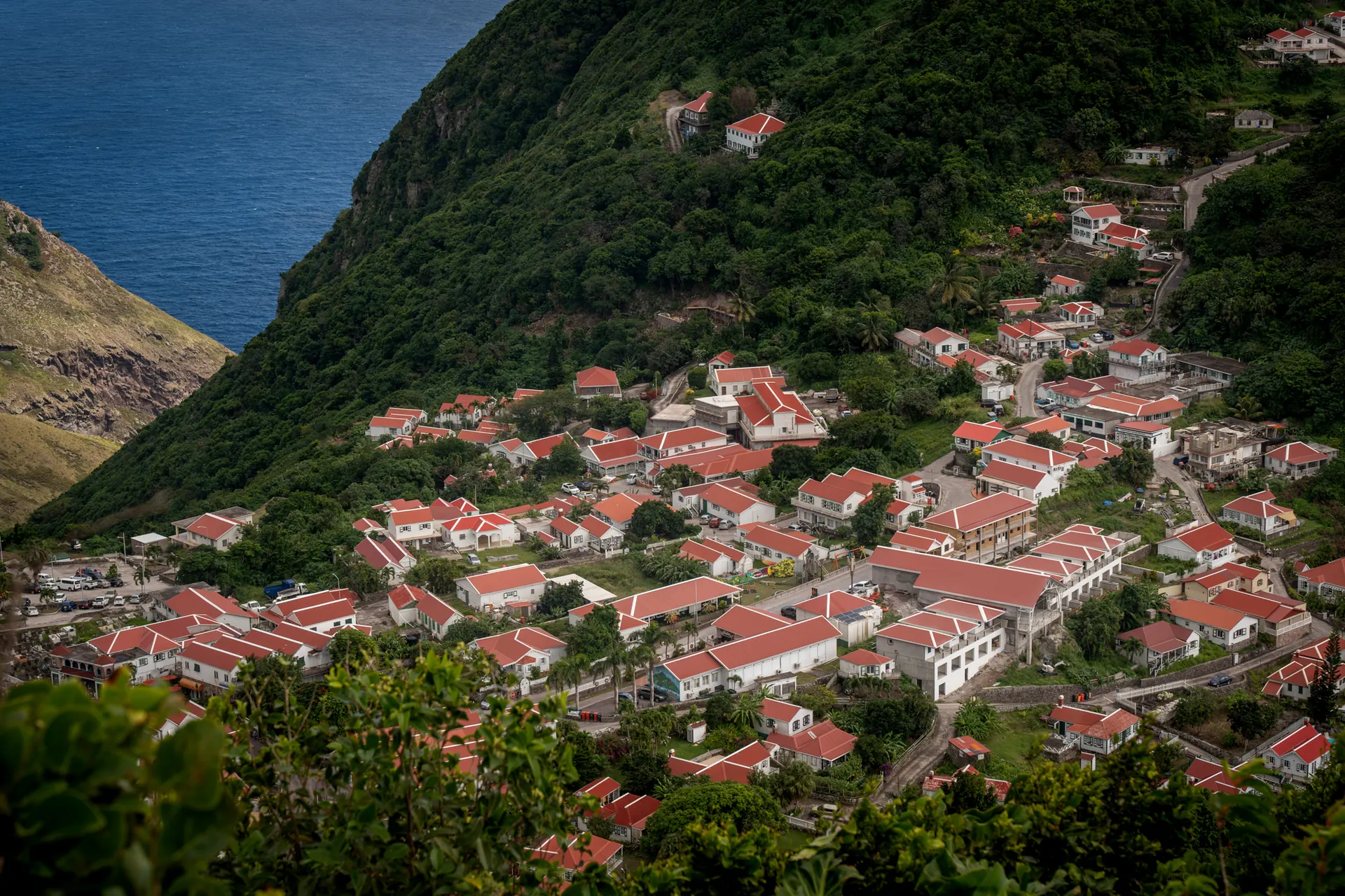 Sunset over Saba, red-roofed houses filling the green valley between the peaks, with the sea beyond